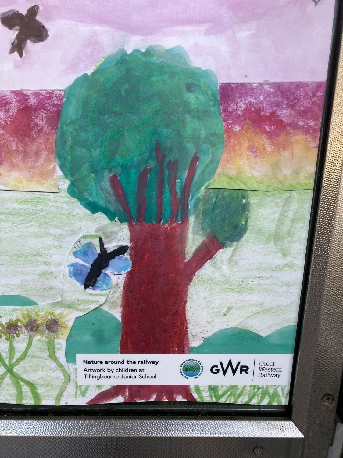 Close-up of a painted tree with the Nature around the railway credit label for Tillingbourne Junior School, Southeast Communities Rail Partnership and Great Western Railway